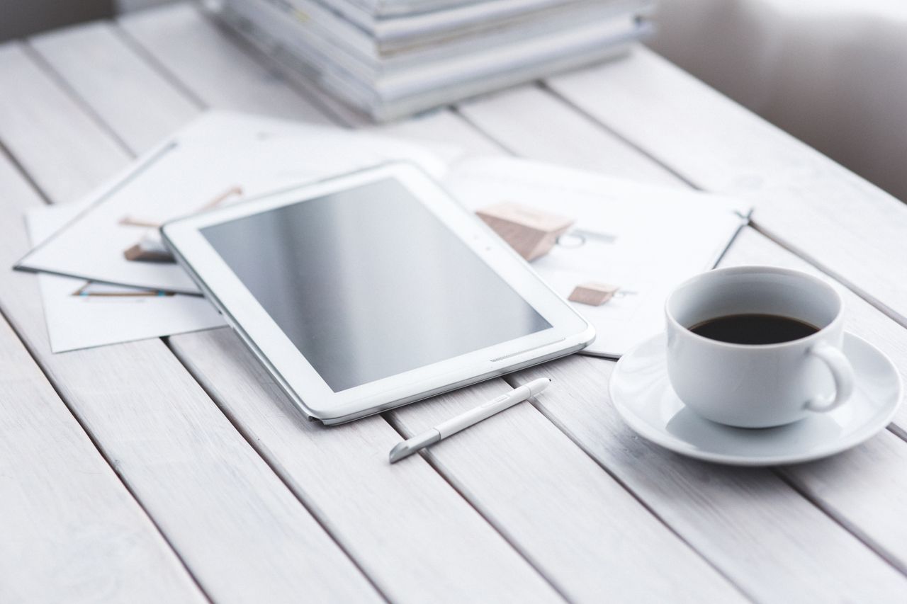 About White tablet with stylus and coffee cup on modern office desk setup.