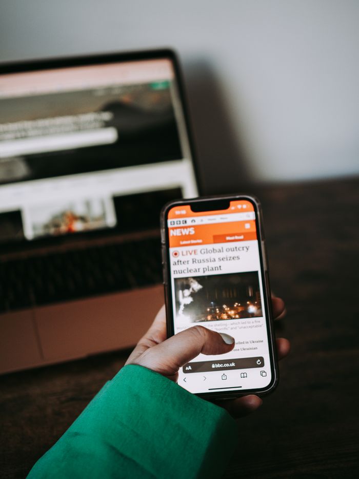 Home Person using smartphone for reading news online with laptop in background.