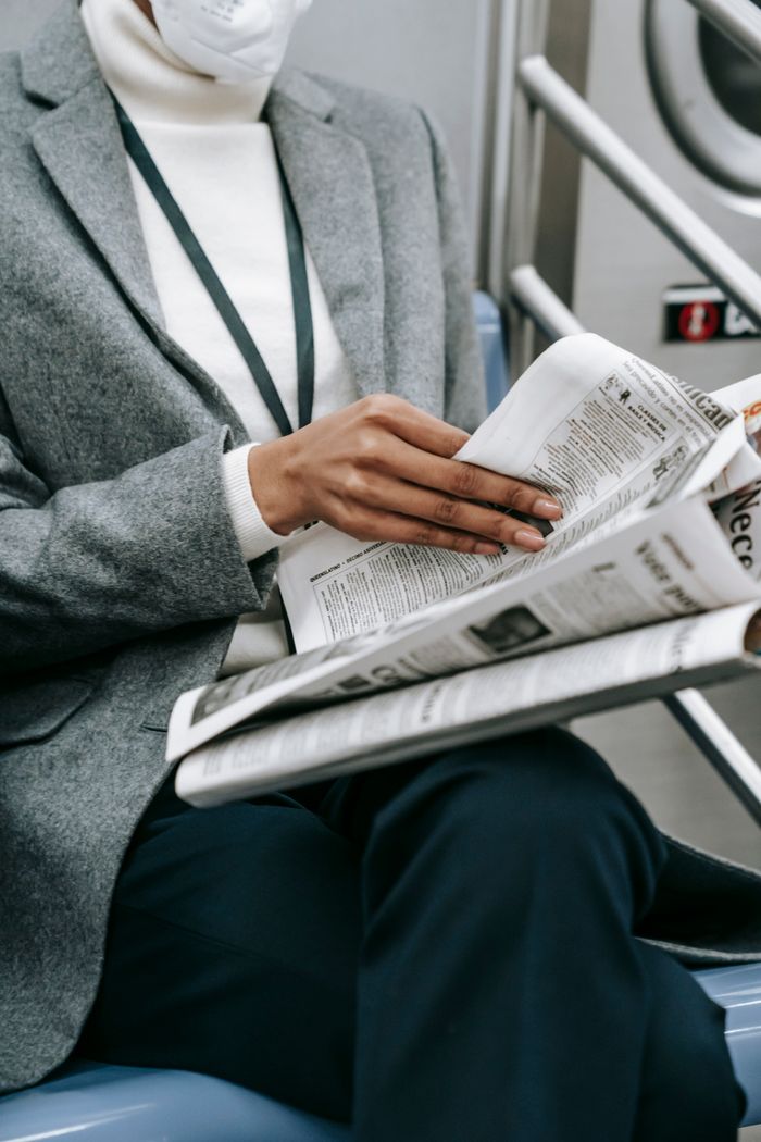 Offerings Crop anonymous black female entrepreneur in elegant outfit and medical mask reading newspaper while riding train